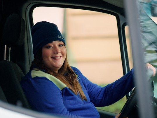 A GLS driver sits in the delivery van and smiles at the camera
