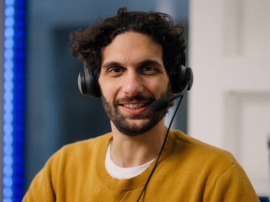 A GLS service employee wearing a headset smiles at the camera