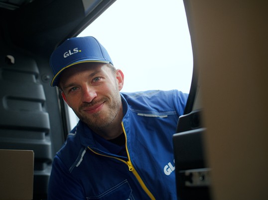 A GLS employee in work clothes smiles at the camera